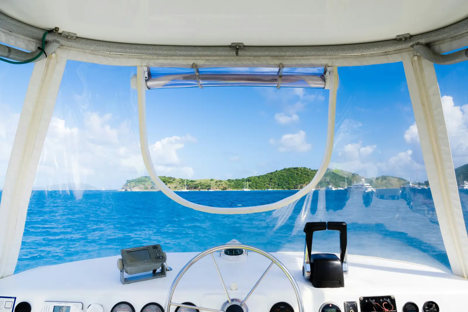 Helm and screens at a boat's console, with a green island offshore