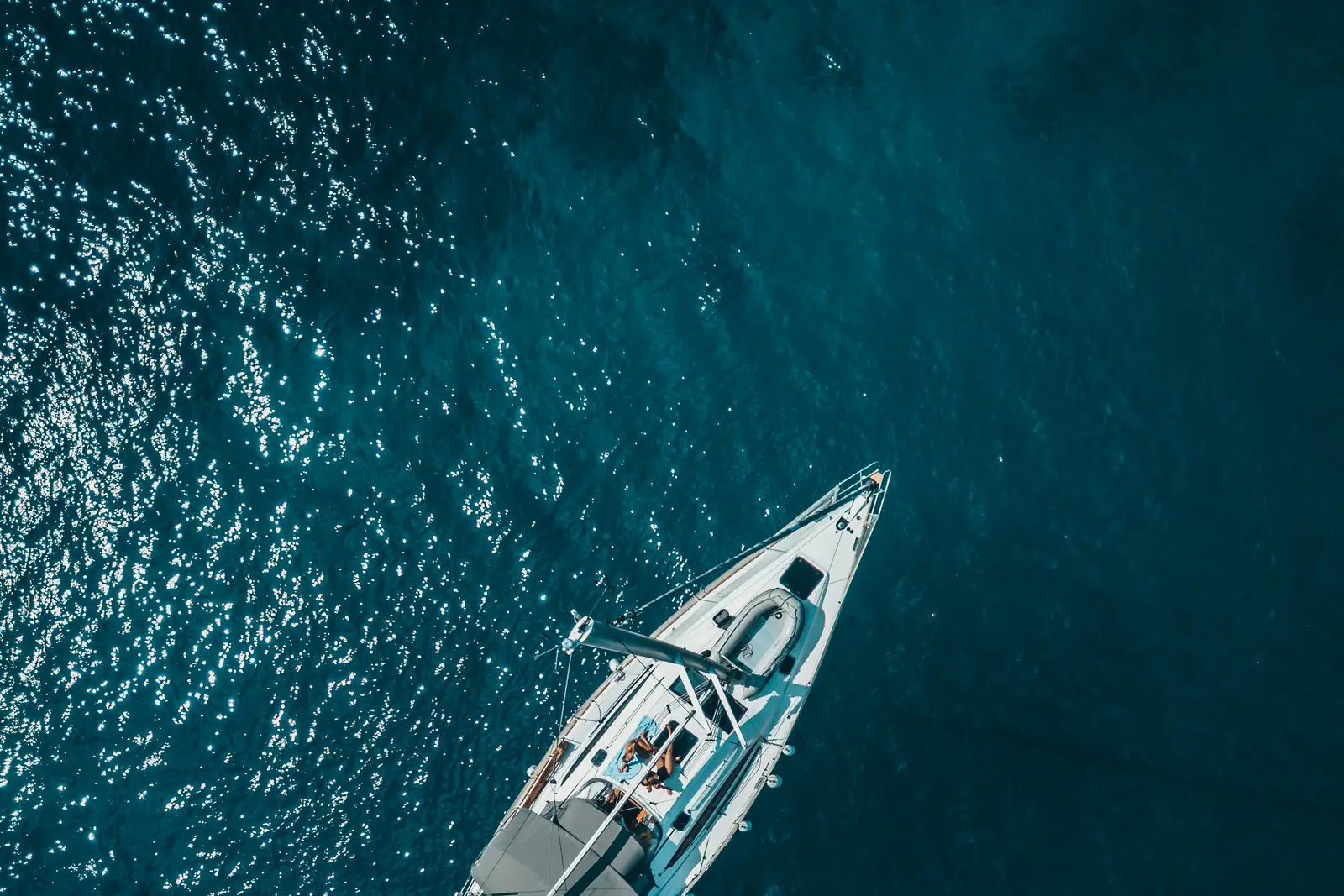 Sailboat moving through deep turquoise water, from above