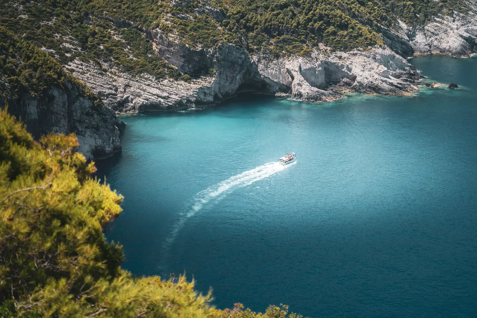 Boat moving through turquoise water in a rocky cove